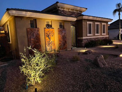 Three metal privacy screen panels with leaf cutouts leaning against a stucco house at dusk on Tampa Home & Garden Store