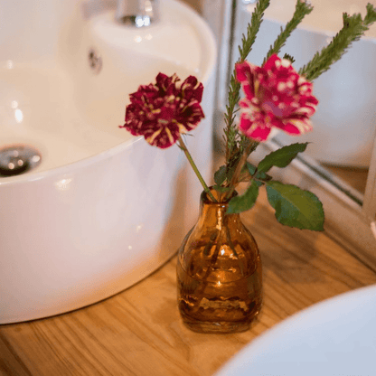 Amber handblown glass vase by RusticReach with two pink and maroon flowers on a wooden surface on Tampa Home & Garden Store