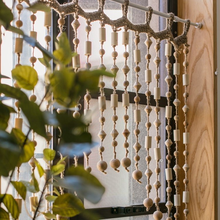 Wood Beaded Door Curtain with natural wooden beads hanging by a sunlit window on Tampa Home & Garden Store
