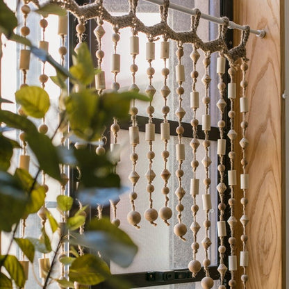 Wood Beaded Door Curtain with natural wooden beads hanging by a sunlit window on Tampa Home & Garden Store