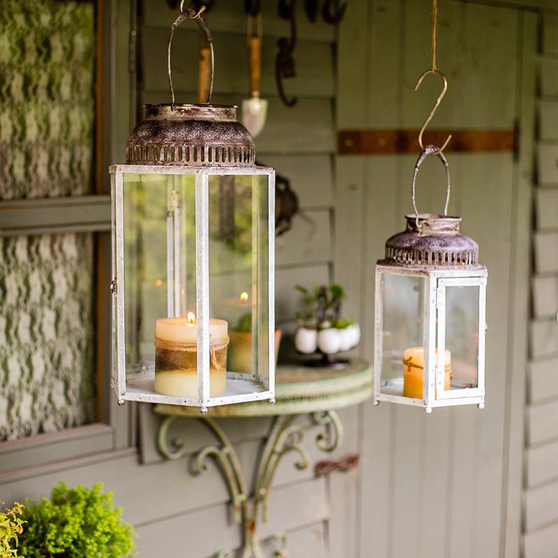 Two hanging glass metal lantern candle holders with distressed white frames and lit candles on Tampa Home & Garden Store