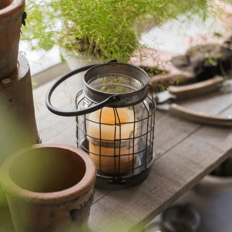 European Restoration Candle Holder in black metal cage with glass insert and amber candle on wood on Tampa Home & Garden Store