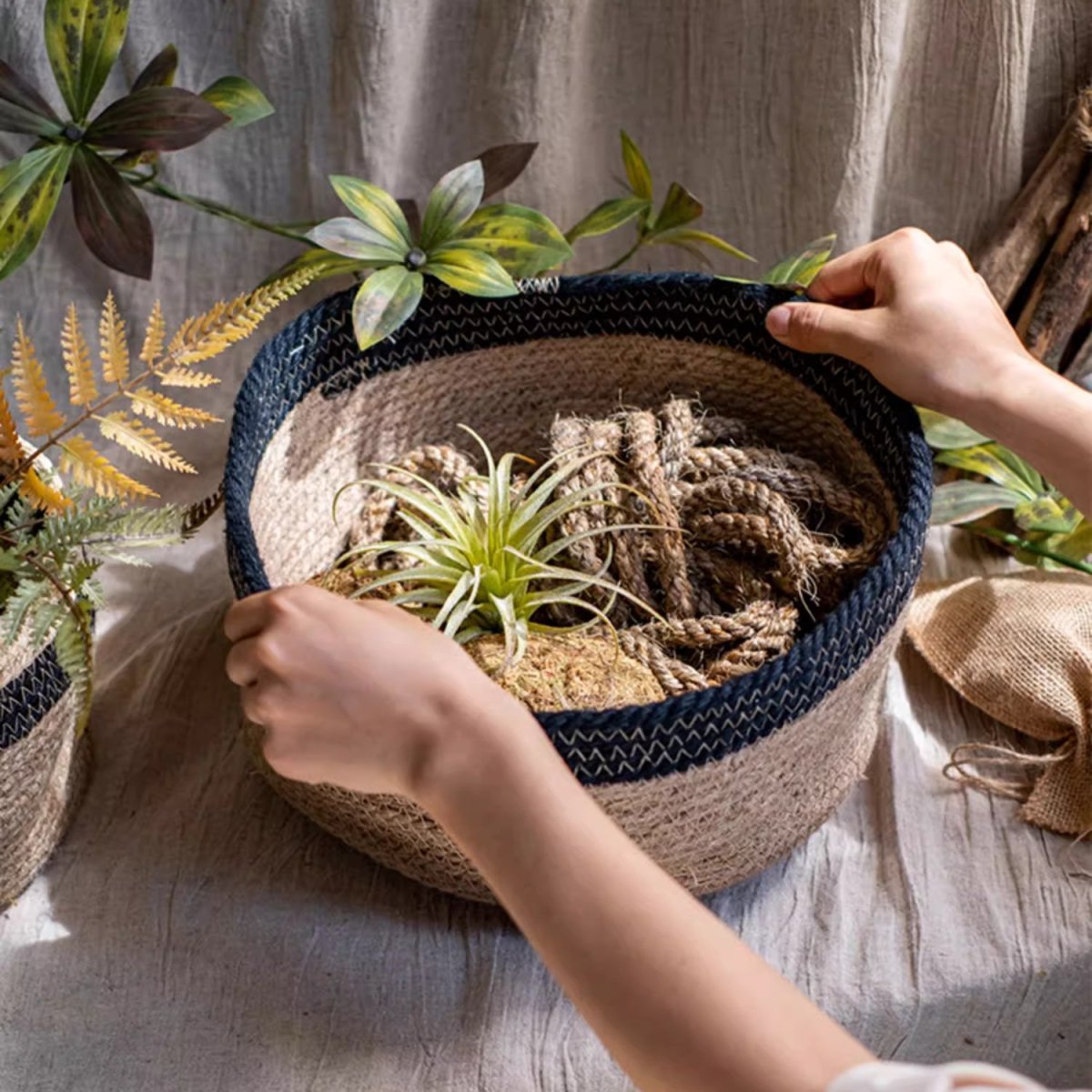 Cotton Blend Woven Storage Basket beige body with navy rim RusticReach brand, hands hold open basket on Tampa Home & Garden Store