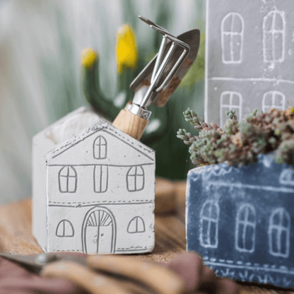 Two TinyHome clay planters by RusticReach; white house pot with a trowel, blue planter nearby on Tampa Home & Garden Store