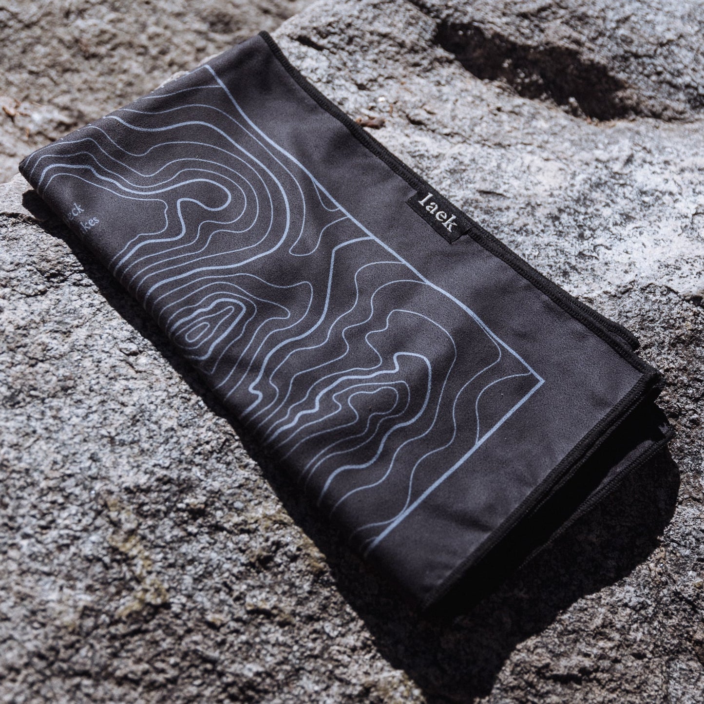 Terrain Towel Laek in charcoal with light blue contour-map print, folded on rocky surface on Tampa Home & Garden Store