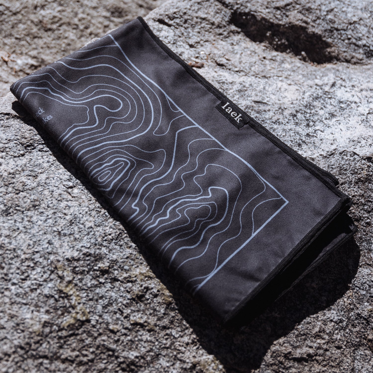 Terrain Towel Laek in charcoal with light blue contour-map print, folded on rocky surface on Tampa Home & Garden Store