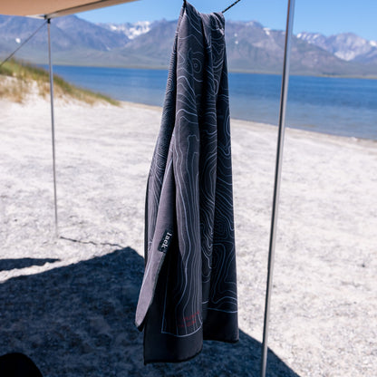 Terrain Towel by Laek, dark gray with contour lines, hanging from a canopy at a lakeside beach on Tampa Home & Garden Store