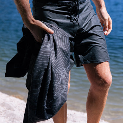 Terrain Towel by Laek, dark navy striped beach towel held by a man near the water on Tampa Home & Garden Store