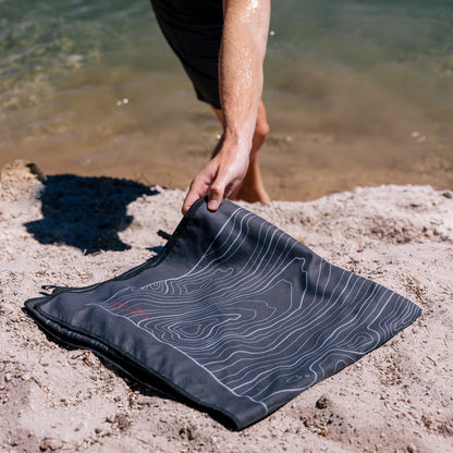 Terrain Towel by Laek with topographic line print laid on sandy shore by water on Tampa Home & Garden Store