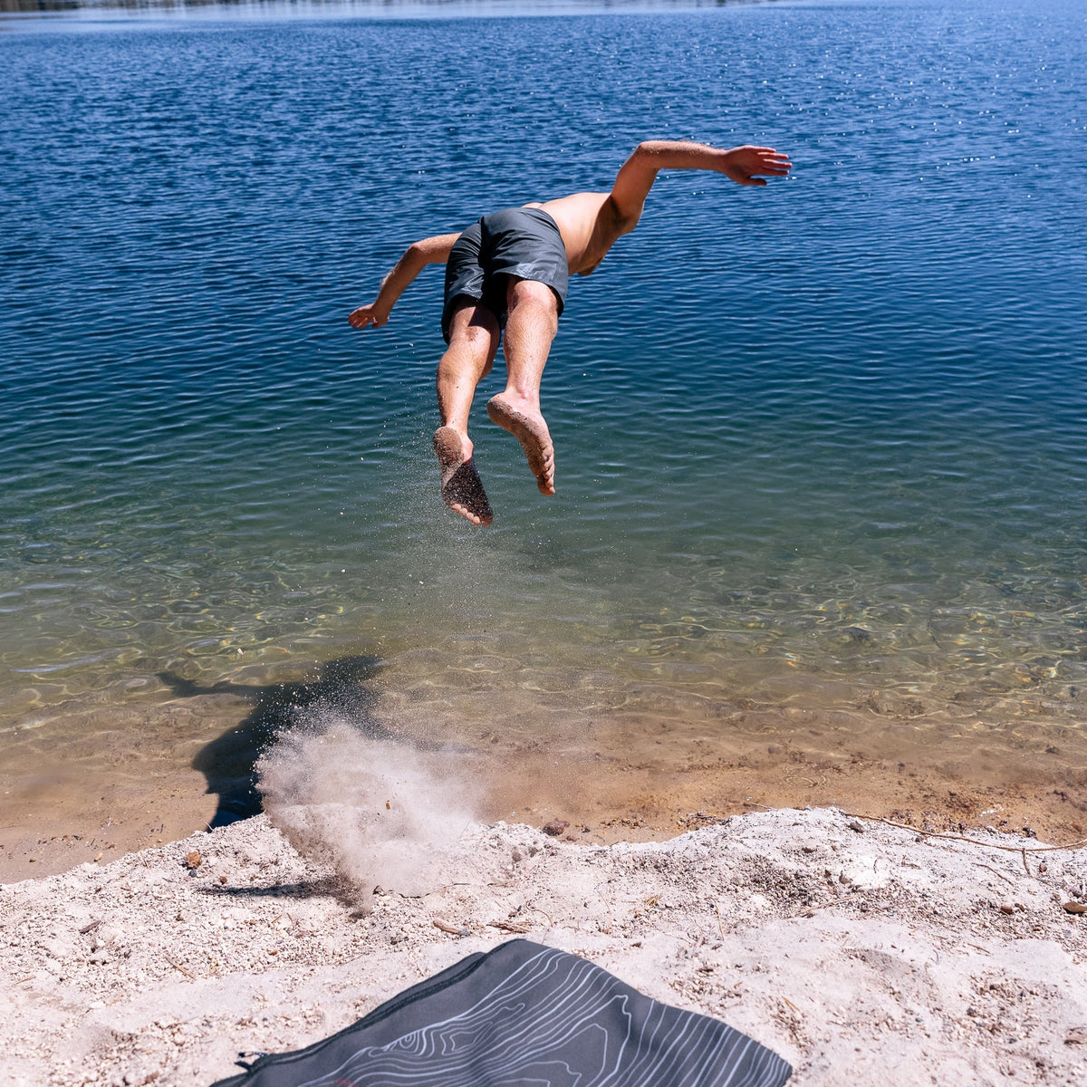 Terrain Towel by Laek, dark striped beach towel on sandy shore beside clear blue water on Tampa Home & Garden Store