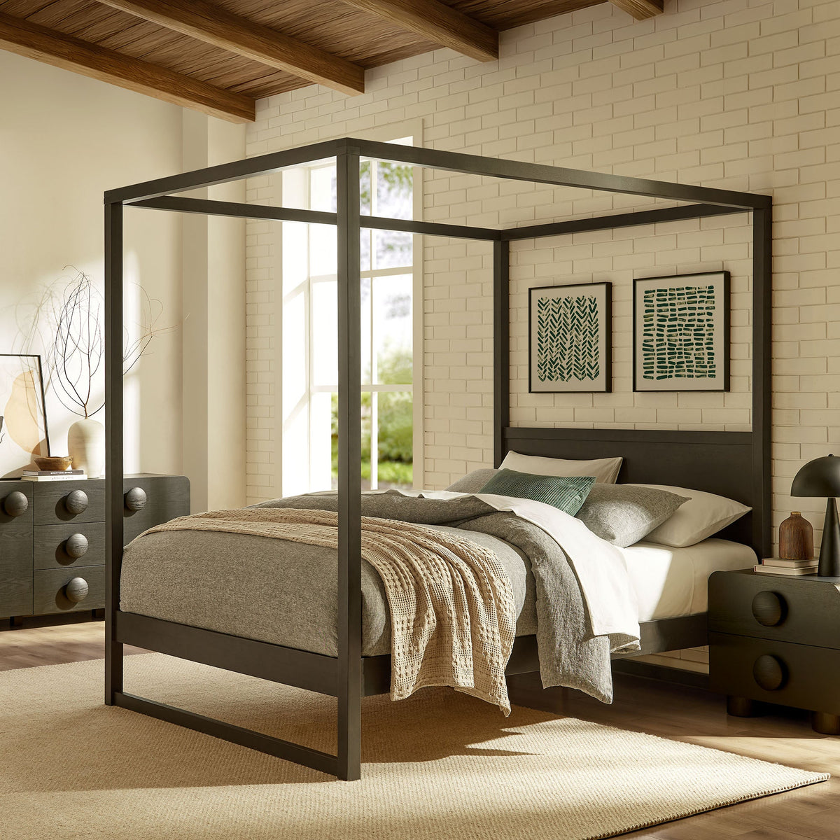 Alva King canopy bed frame in dark metal with platform base and bedding against white brick wall on Tampa Home & Garden Store