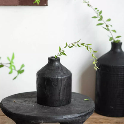 Two black wooden vases with narrow necks on a round table, green leafy stems on Tampa Home & Garden Store