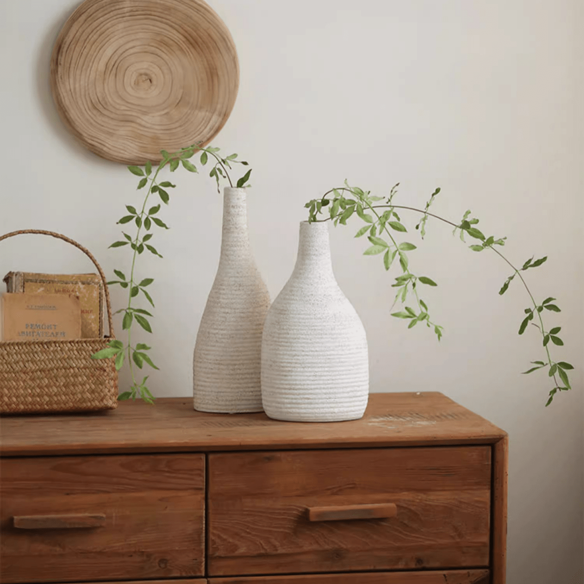 Narrow-neck white vases with textured finish and trailing greenery on a wooden dresser on Tampa Home & Garden Store