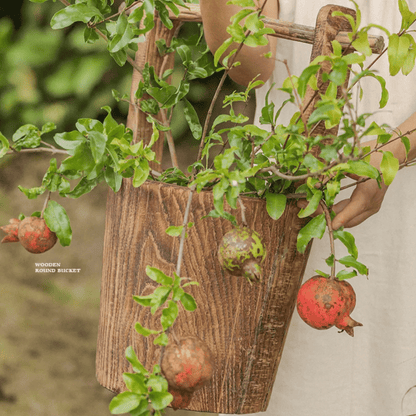 Old-fashioned wooden round bucket with natural wood grain, greenery and hanging pomegranate fruit on Tampa Home & Garden Store