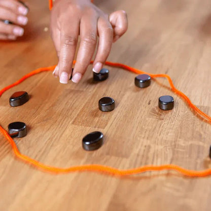 Magnetic Travel Chess Set black round pieces scattered on a wooden table with an orange cord outline on Tampa Home & Garden Store