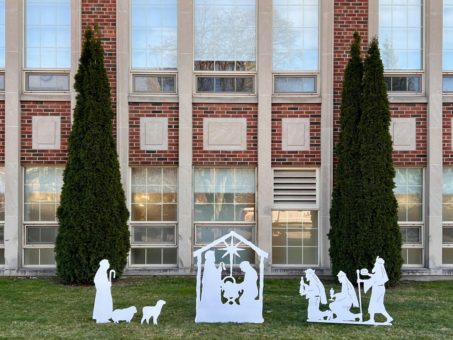 Nativity Scene Outdoor white yard silhouettes displayed on green lawn before brick building windows on Tampa Home & Garden Store