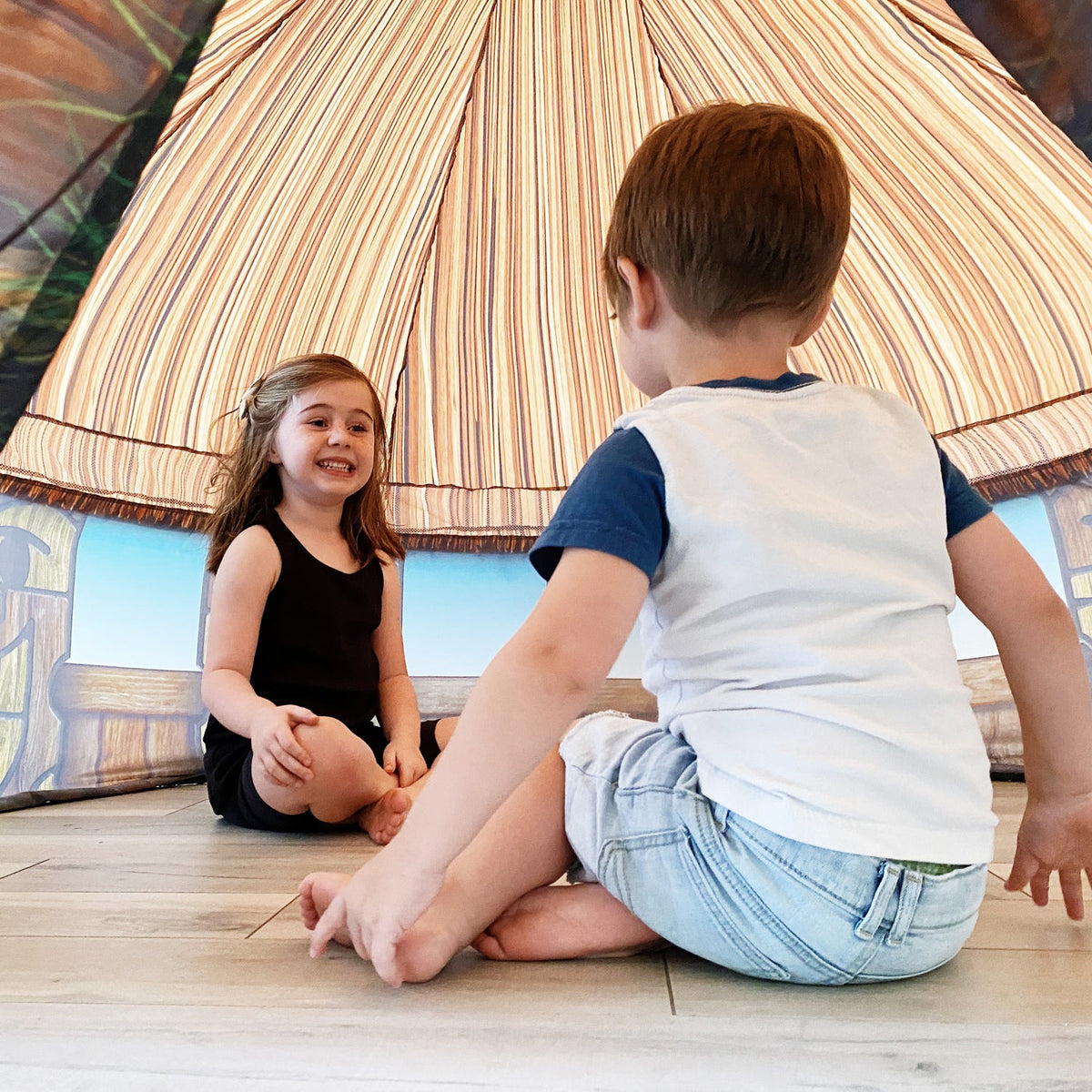 AirFort Tiki Hut inflatable play fort with striped canopy, two kids inside on wooden floor on Tampa Home & Garden Store