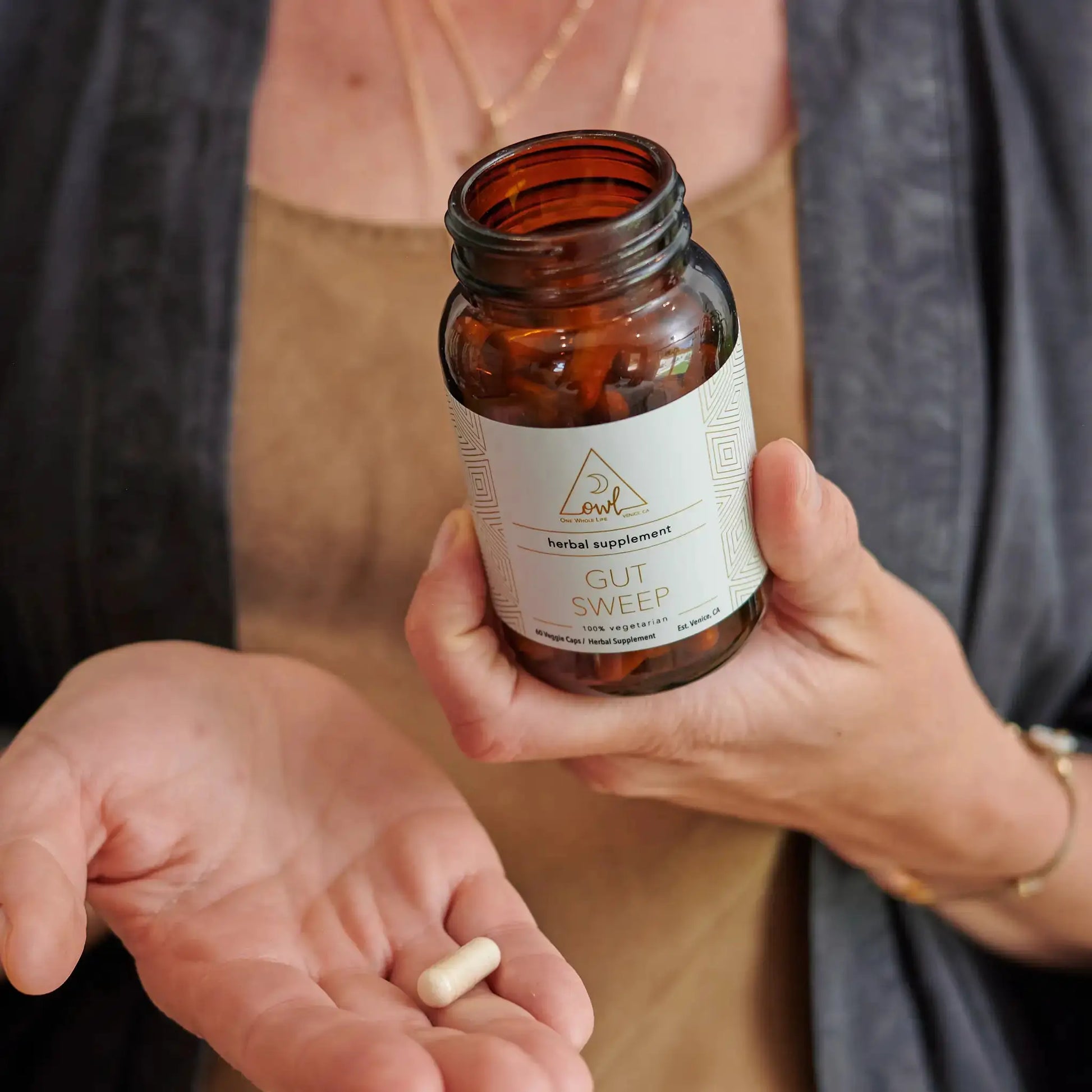 Gut Sweep digestive supplement bottle OWL Venice; amber bottle with two capsules in hand on Tampa Home & Garden Store