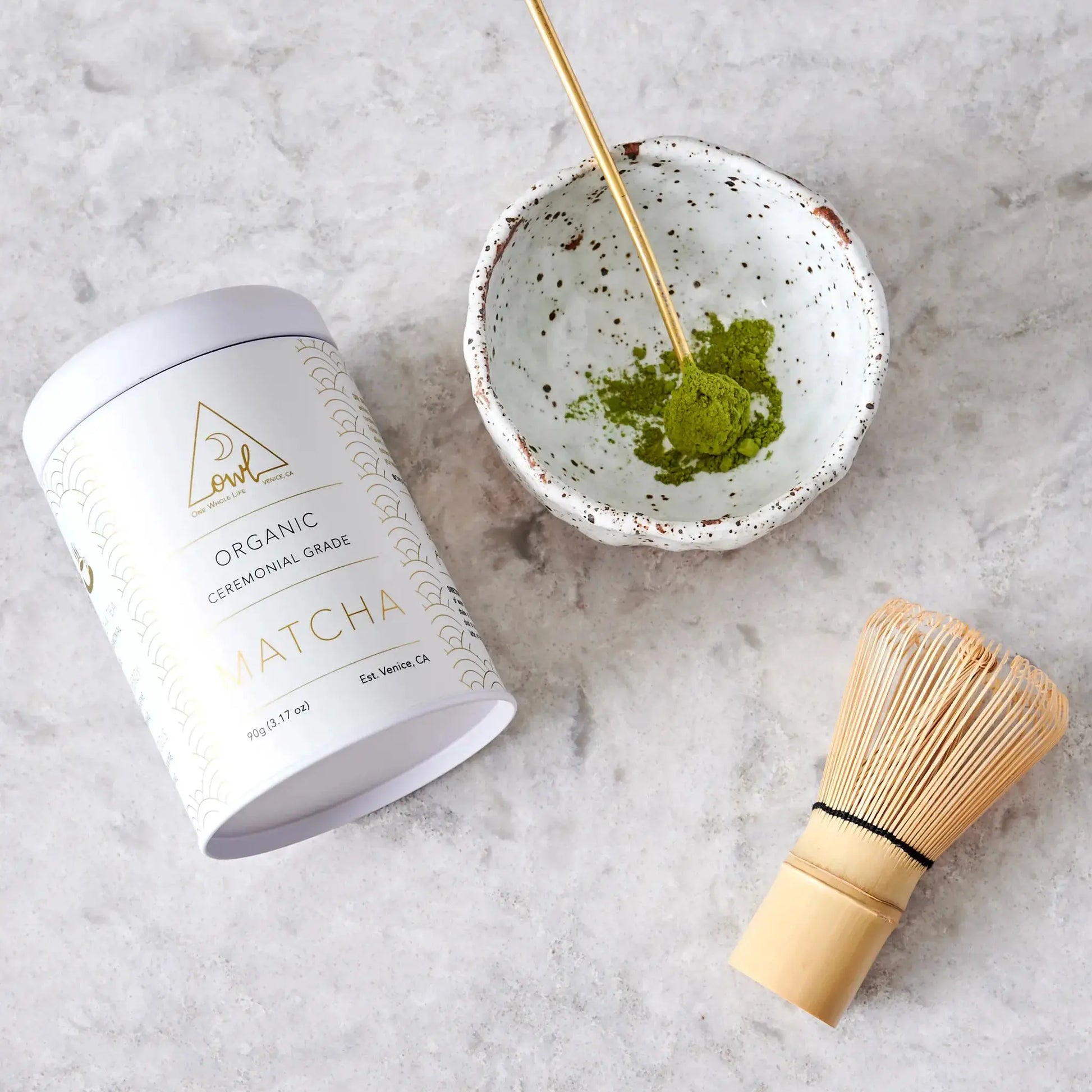 Organic matcha powder OWL Venice in jar with gold pattern beside bowl and bamboo whisk on Tampa Home & Garden Store