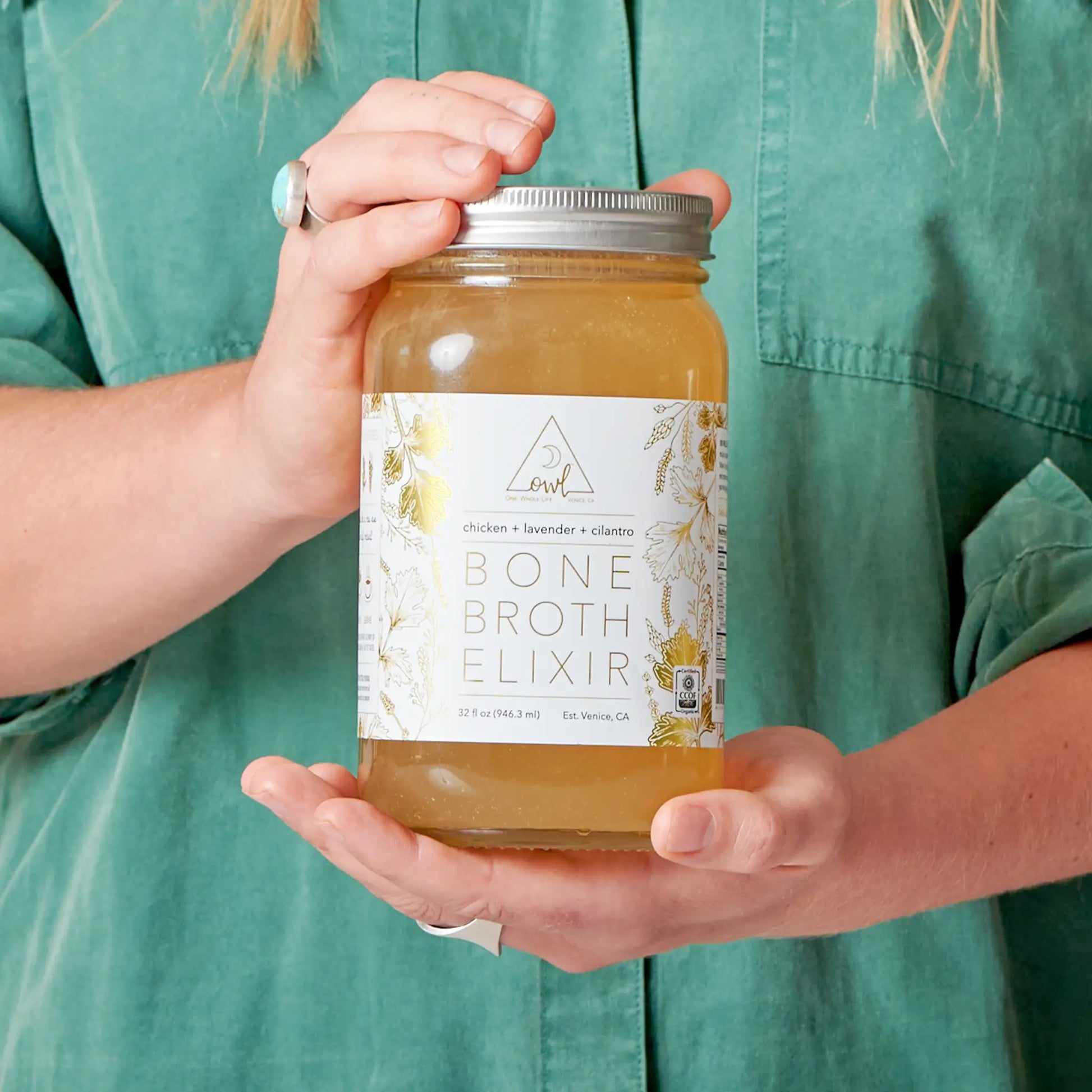 Organic chicken bone broth elixir bottle by OWL Venice held in hand with metal lid and label design on Tampa Home & Garden Store