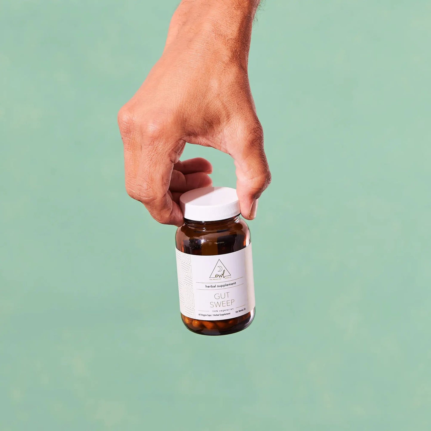 Gut Sweep herbal supplement bottle by OWL Venice held in hand with white twist cap on Tampa Home & Garden Store
