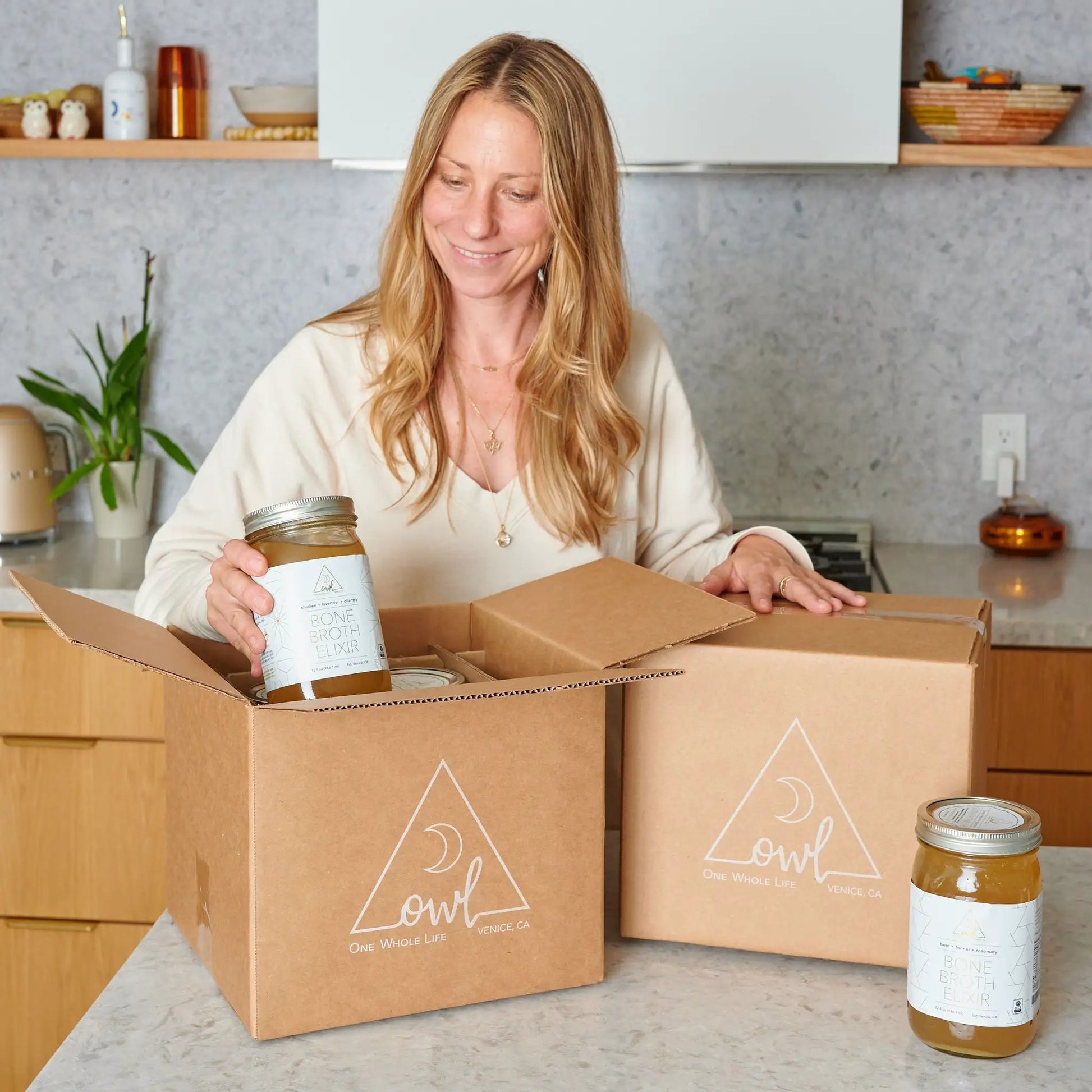 Bone Broth Elixir bottle by OWL Venice in an open box, golden broth visible in kitchen on Tampa Home & Garden Store