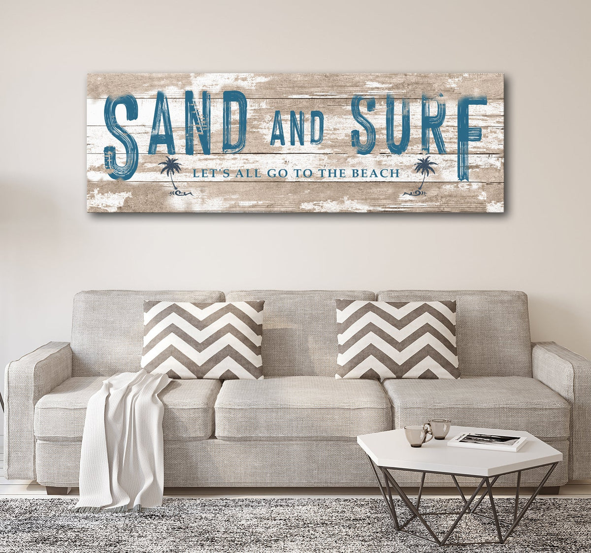 Sand And Surf canvas sign with distressed wood, blue lettering and palm icons over a beige sofa on Tampa Home & Garden Store