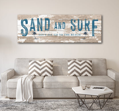 Sand And Surf canvas sign with distressed wood, blue lettering and palm icons over a beige sofa on Tampa Home & Garden Store