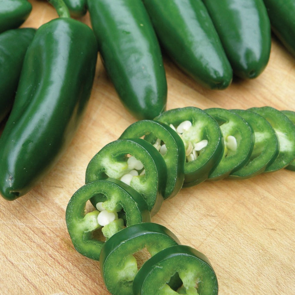 Jalapeno Early Pepper seeds, multiple green jalapeños with sliced rings and seeds on wood board on Tampa Home & Garden Store