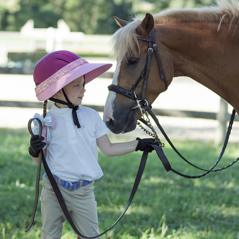 EquiVisor Glitz sun visor in pink with glitter band worn by child beside a horse on Tampa Home & Garden Store