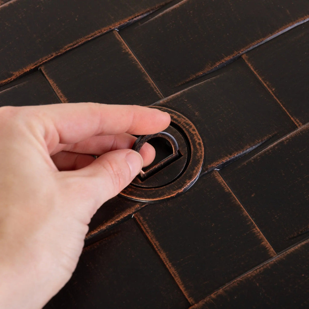 Perissa woven aluminum LPG fire pit ring being grasped by fingers on a dark brown woven surface on Tampa Home & Garden Store