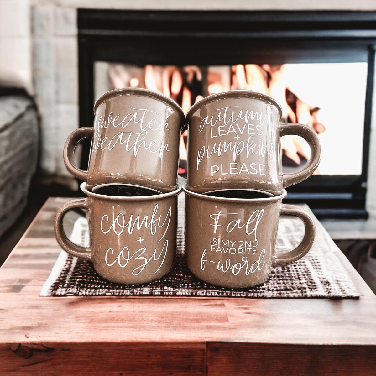 Gia Roma Autumn Leaves mugs, four taupe ceramic mugs with white script, stacked by a fireplace on Tampa Home & Garden Store