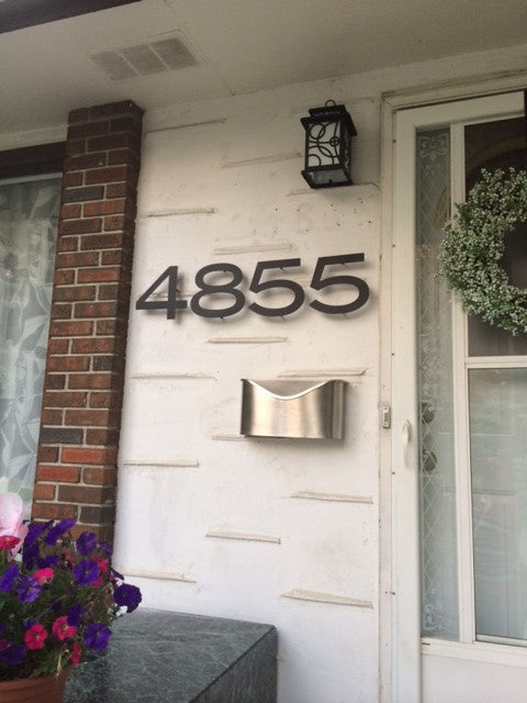 Rustic house number digits 4855 in metal by Rustica Ornamentals mounted on white stucco wall by front door on Tampa Home & Garden Store