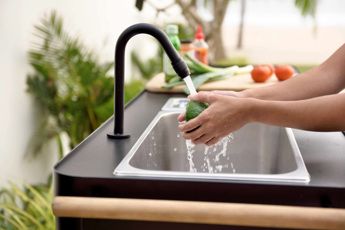 Portals Dark Outdoor Kitchen sink with black matte faucet; hands washing a green bell pepper on Tampa Home & Garden Store