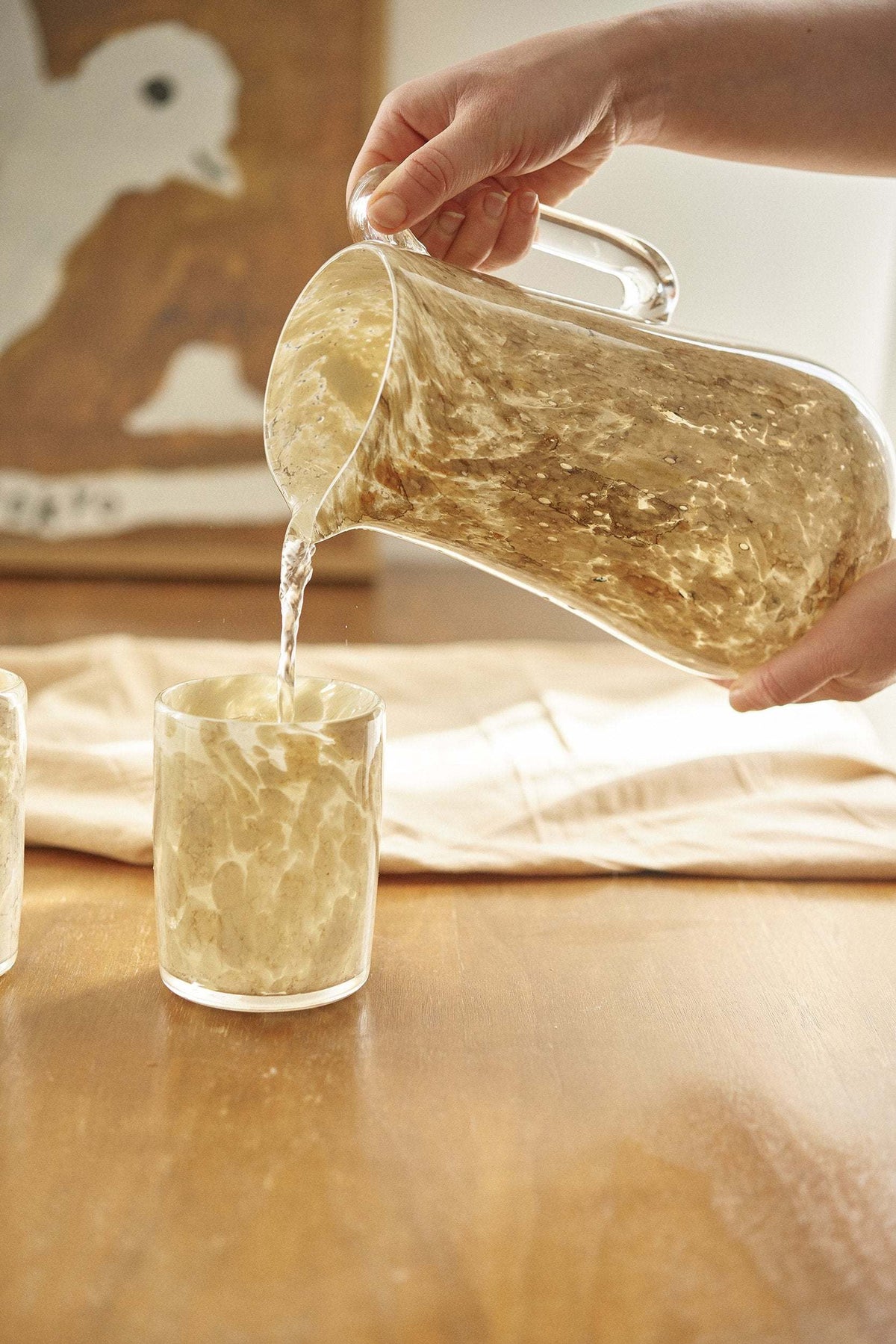Two hand blown glass tumblers with beige marble pattern, poured from a clear glass pitcher on Tampa Home & Garden Store