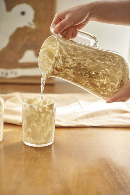 Two hand blown glass tumblers with beige marble pattern, poured from a clear glass pitcher on Tampa Home & Garden Store