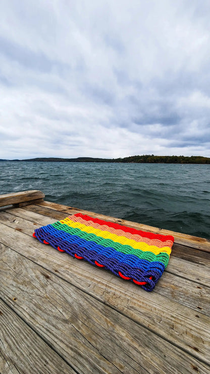 Rainbow lobster rope welcome mat with vibrant rainbow stripes on a dock beside the water on Tampa Home & Garden Store