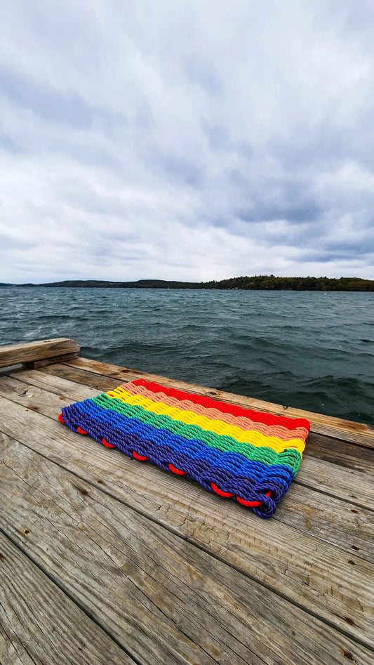 Rainbow lobster rope welcome mat with vibrant rainbow stripes on a dock beside the water on Tampa Home & Garden Store