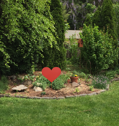 Red metal heart garden stake by Rustica Ornamentals in a rock-bordered garden with potted plants on Tampa Home & Garden Store