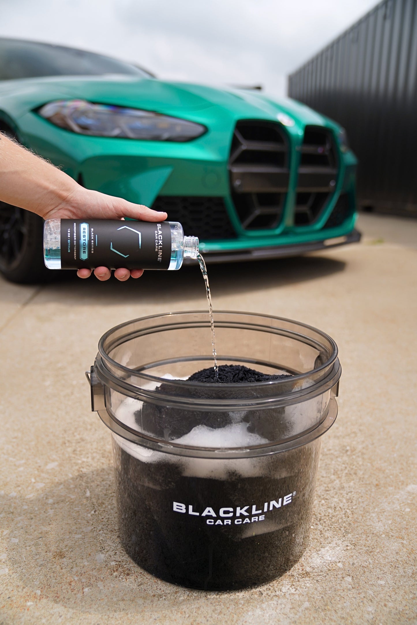 Blackline Restore microfiber detergent bottle poured into a wash bucket with a green car behind on Tampa Home & Garden Store