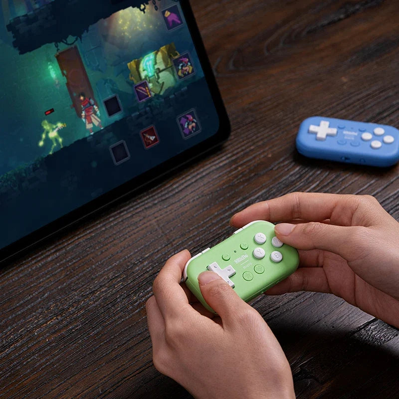 8BitDo Micro Bluetooth Wireless Gamepad, green in hand, blue pad on desk with tablet gameplay on Tampa Home & Garden Store