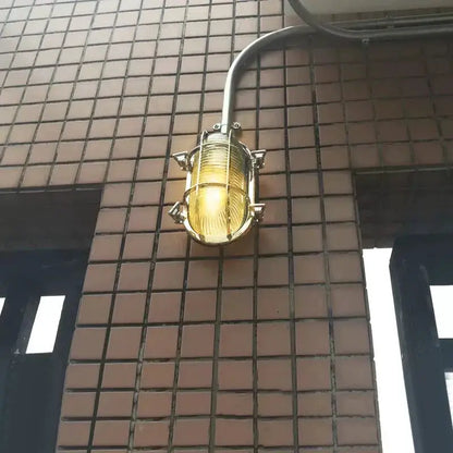 Industrial outdoor wall lamp by DecorBites with brass cage amber LED glow on tiled exterior wall on Tampa Home & Garden Store