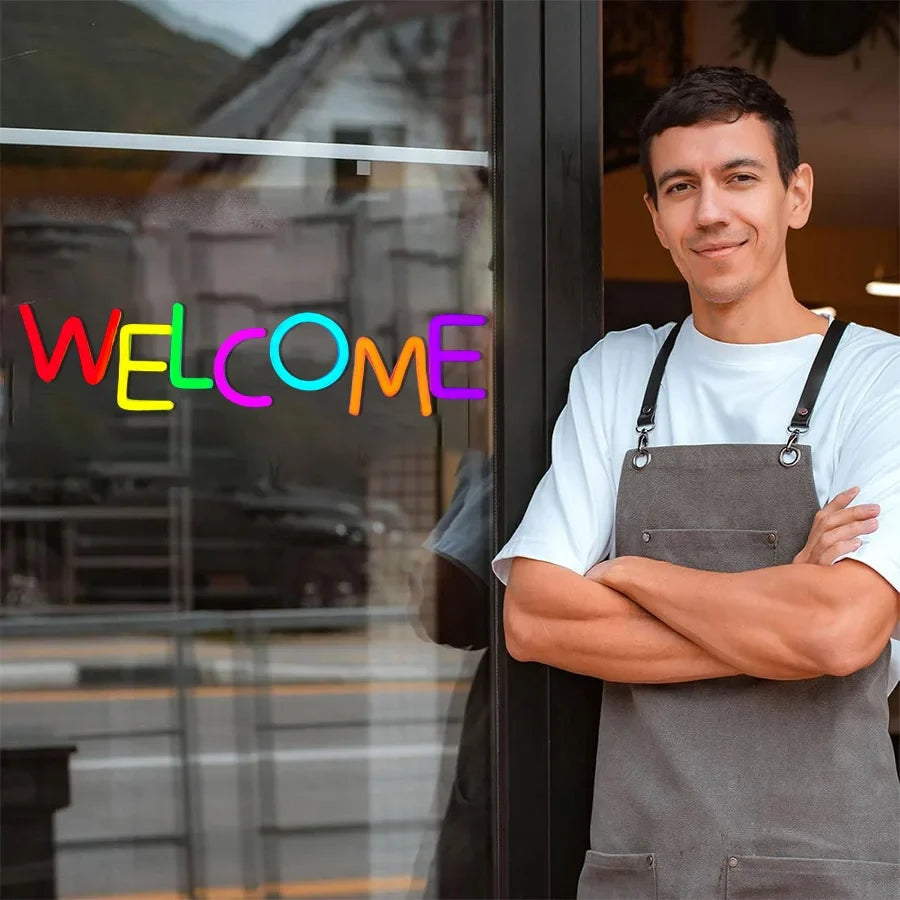 Welcome neon sign with multicolor letters on glass storefront; man in gray apron beside the door on Tampa Home & Garden Store