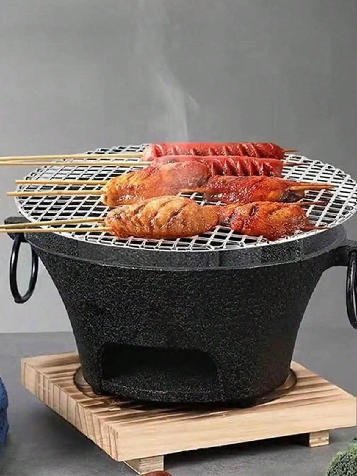 Round black cast-iron charcoal grill with lattice grate and meat skewers cooking on Tampa Home & Garden Store
