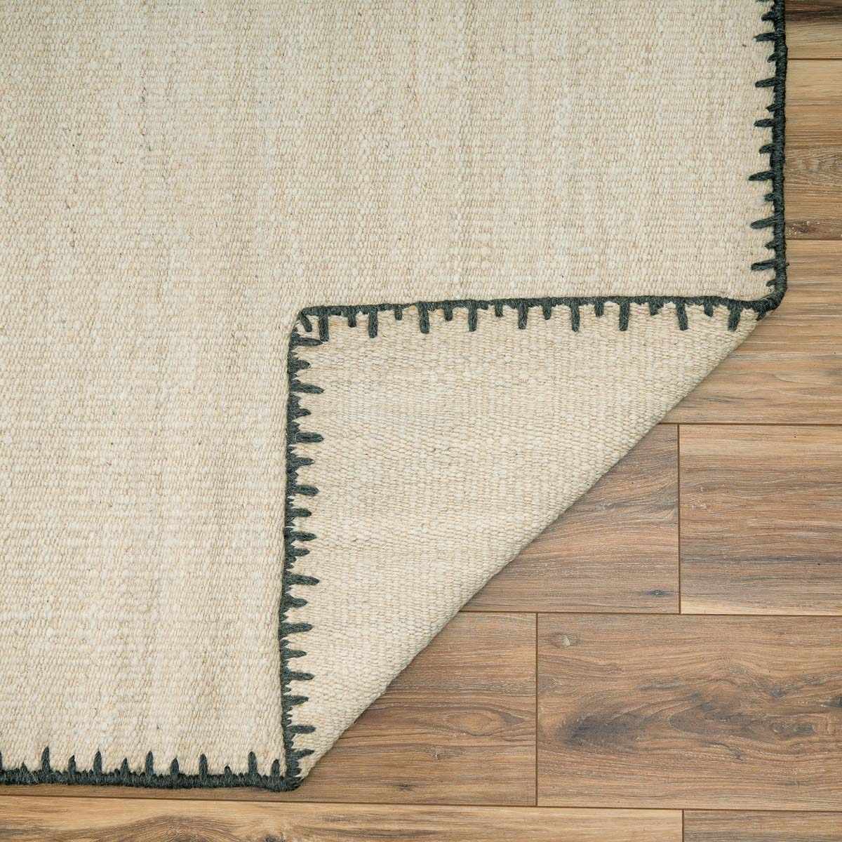 Ayumu Off White Hand Woven Wool Area Rug beige with black border on wood floor, folded on Tampa Home & Garden Store