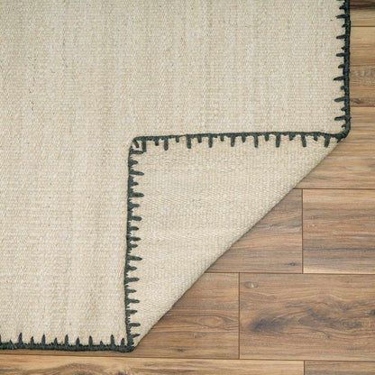 Ayumu Off White Hand Woven Wool Area Rug beige with black border on wood floor, folded on Tampa Home & Garden Store