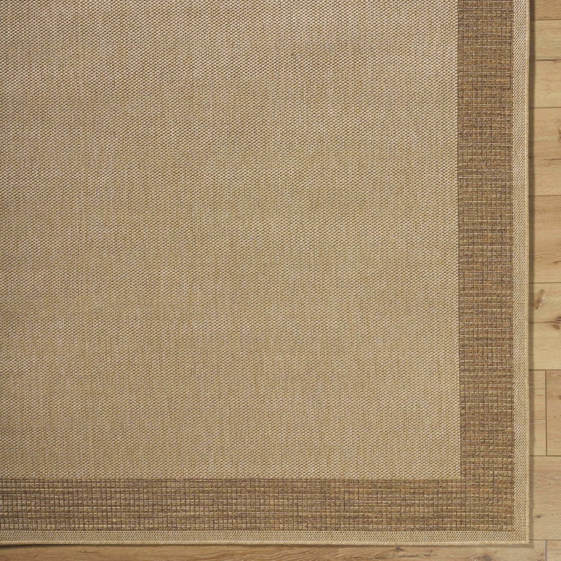 Inigo Flatweave Faux Jute Outdoor Rug, natural beige with brown border on wood floor on Tampa Home & Garden Store