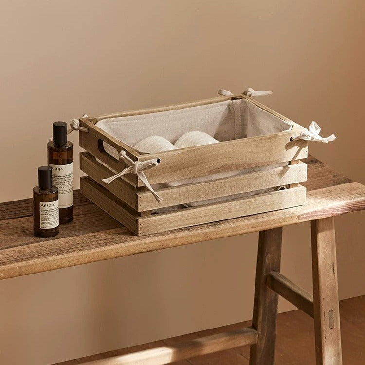 Linen-lined wooden crate with rope-tied sides on a rustic table; contains two white fabric balls on Tampa Home & Garden Store