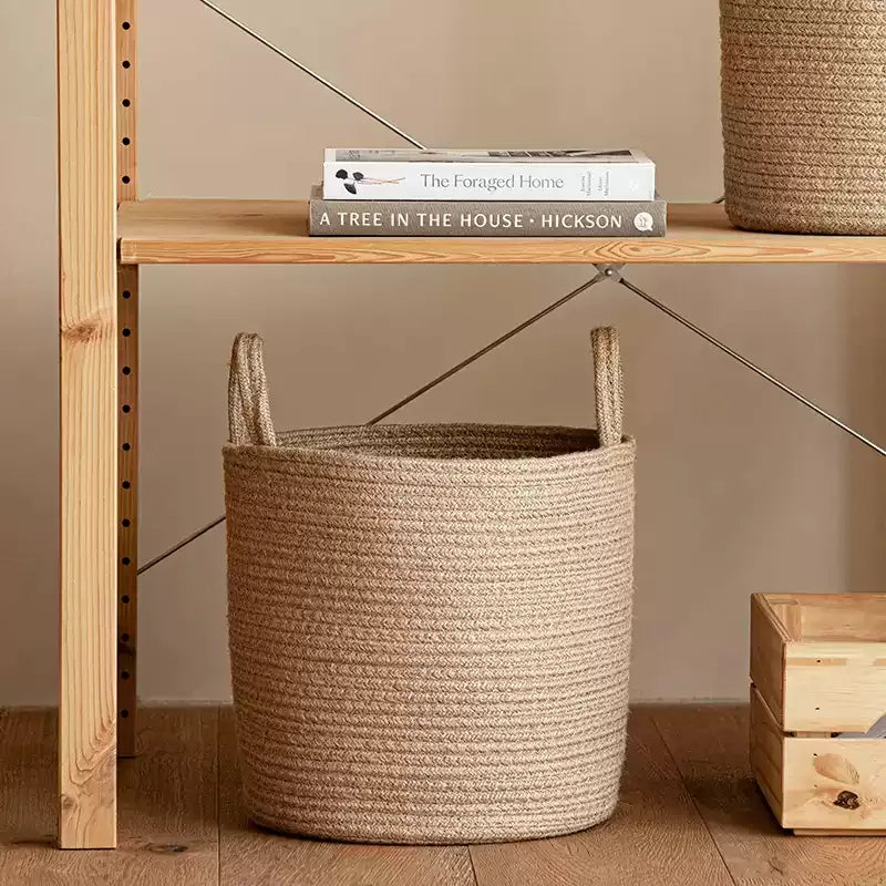 Natural Rope Laundry Basket by RusticReach in beige rope on a wooden shelf beside books on Tampa Home & Garden Store