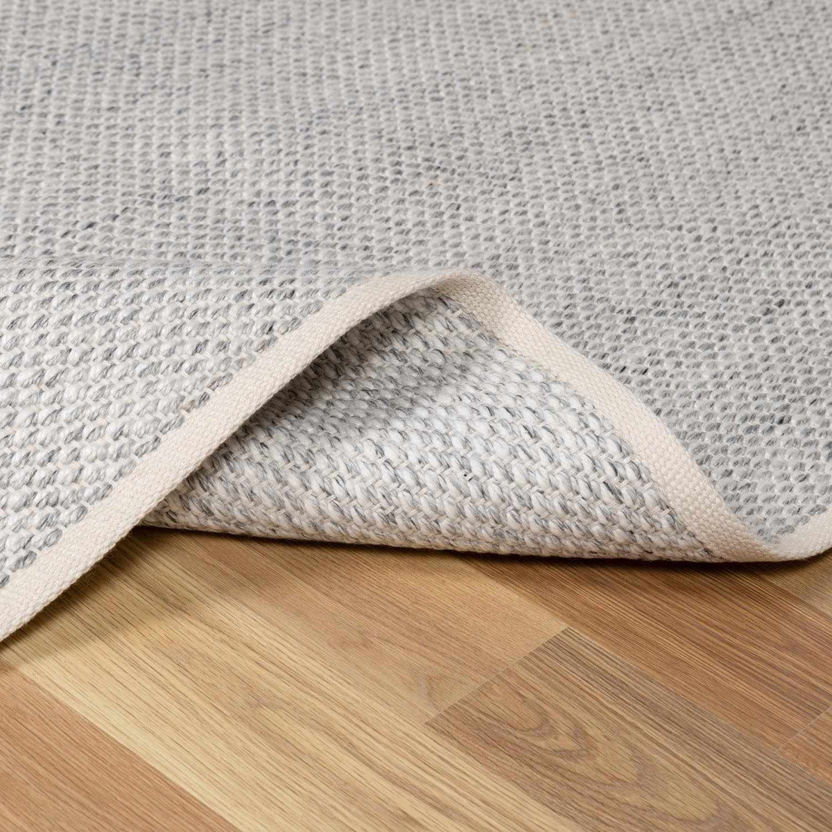 Stenhousemuir Luxe Handmade Rug gray woven texture beige binding Boutique Rugs on wood floor on Tampa Home & Garden Store